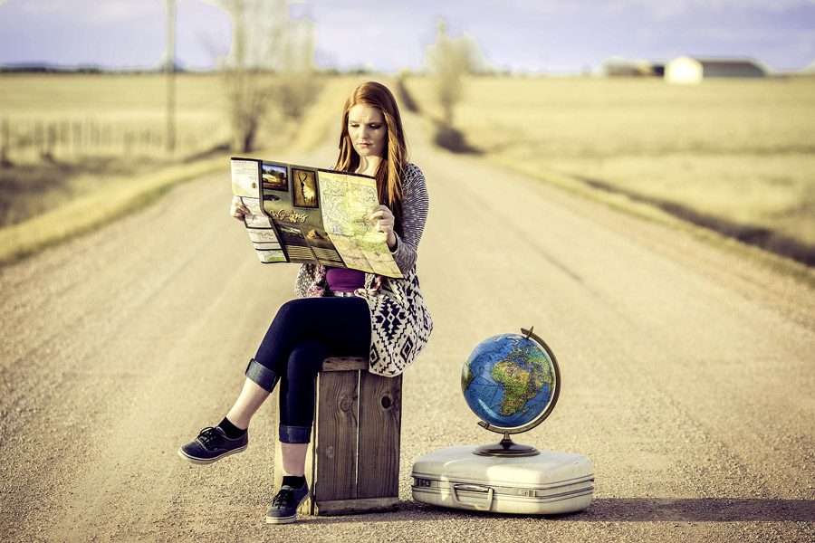 Jeune femme lisant une carte au milieu d'une route déserte